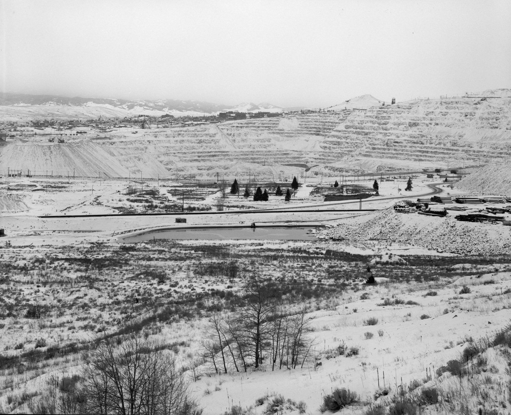 Snow-dusted terraced walls of the Berkeley Pit in Butte, Montana, with the city on the ridge behind