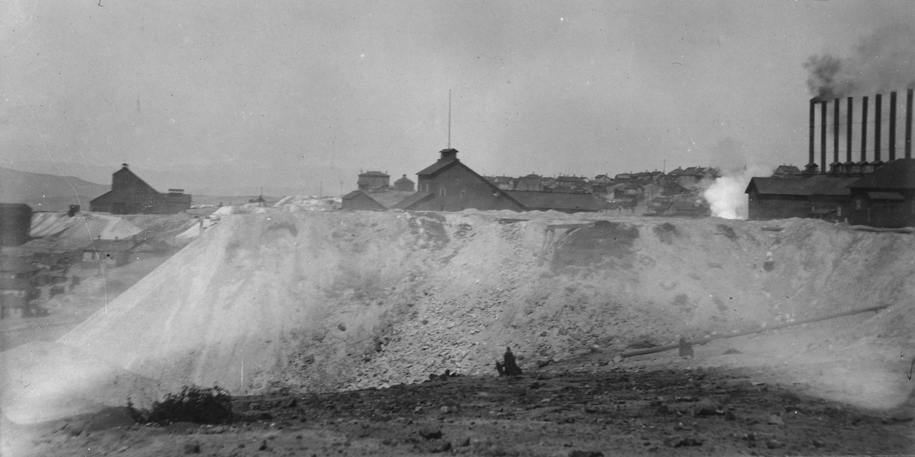 Huge pale tailings pile in front of the Mountain Con mine plant and its row of smokestacks, Butte, 1906
